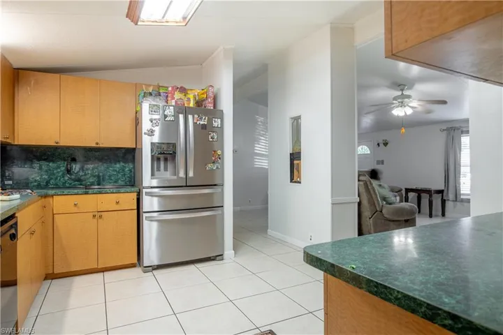 Kitchen with stainless steel refrigerator with ice dispenser, ceiling fan, tasteful backsplash, light tile floors, and lofted ceiling