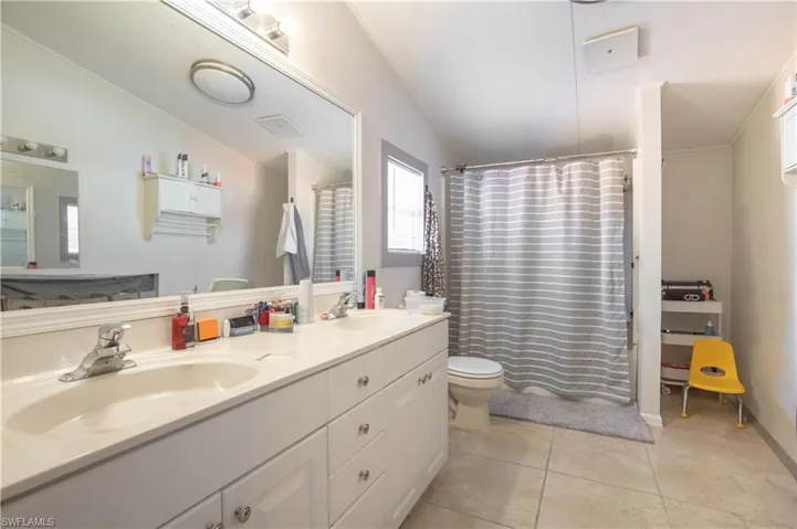 Bathroom featuring dual sinks, tile flooring, oversized vanity, lofted ceiling, and toilet