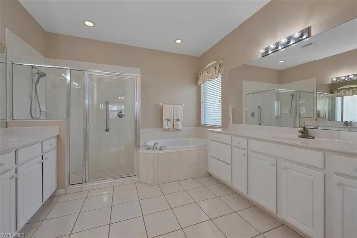 Bathroom featuring a shower stall, two vanities, a bath, light tile patterned floors, and recessed lighting
