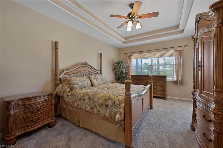 Bedroom with light colored carpet, ceiling fan, and a tray ceiling