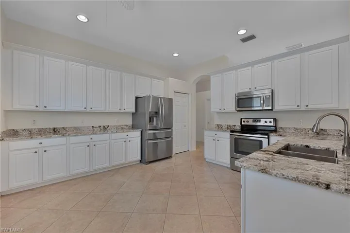 Kitchen with appliances with stainless steel finishes, white cabinetry, light tile patterned floors, light stone countertops, and recessed lighting