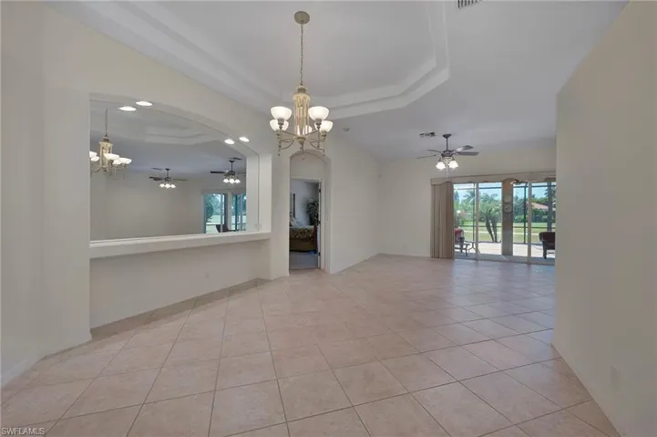 Dining area with a chandelier, ceiling fan, light tile patterned floors, a tray ceiling, and arched walkways