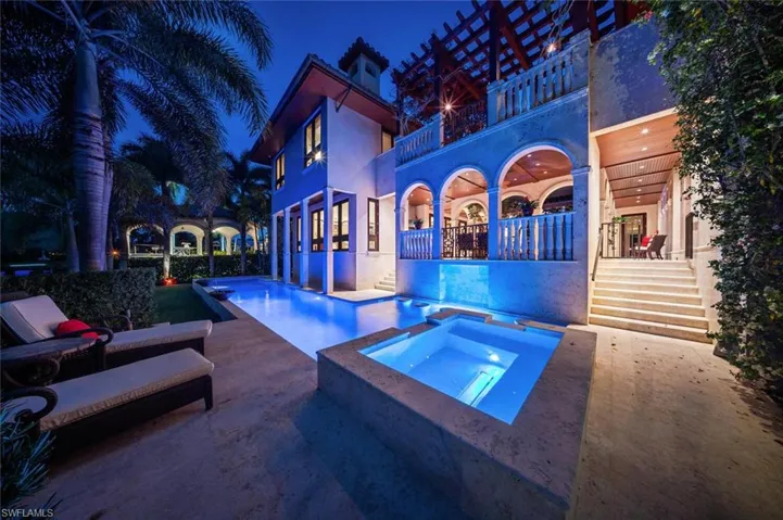 Pool at twilight with a balcony, a patio area, and a pool with connected hot tub