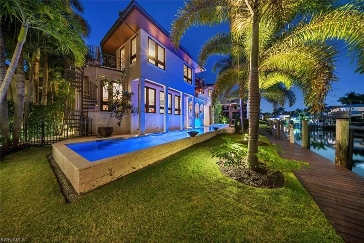 Back of house at night featuring a balcony, stucco siding, a yard, and a water view