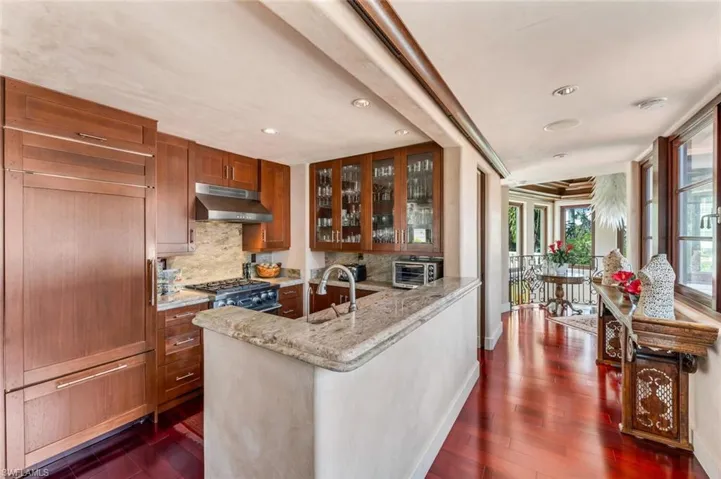 Kitchen with backsplash, glass insert cabinets, brown cabinets, light stone countertops, and paneled built in fridge
