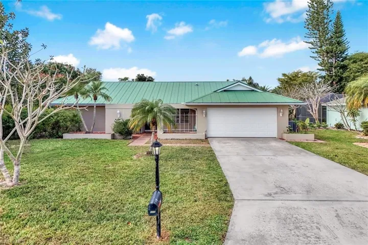 Ranch-style home featuring concrete driveway, a front yard, an attached garage, and a metal roof