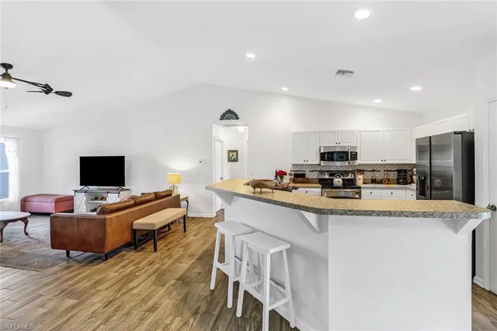 Kitchen featuring stainless steel appliances, lofted ceiling, a breakfast bar, light wood-style floors, and white cabinets