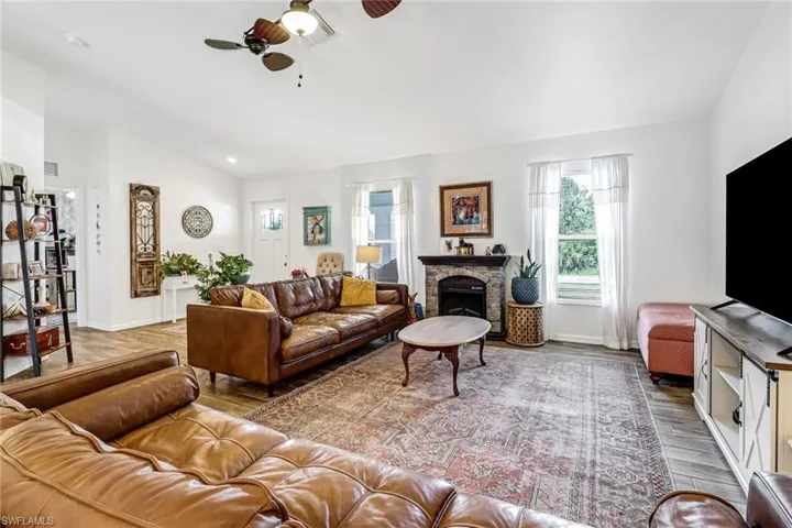 Living room featuring ceiling fan, wood finished floors, a stone fireplace, lofted ceiling, and recessed lighting