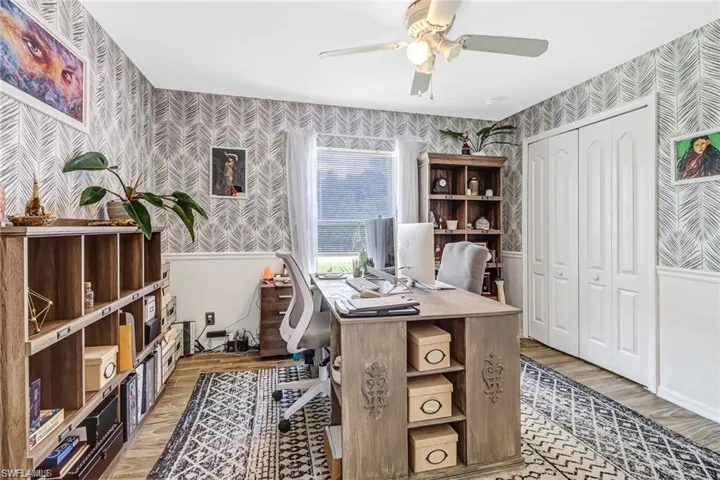 Home office featuring wallpapered walls, light wood finished floors, ceiling fan, and a wainscoted wall