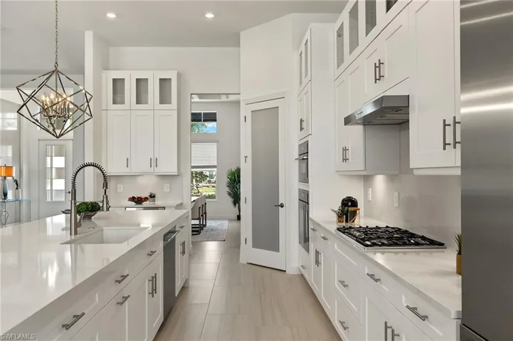 Gourmet Kitchen w/ luxury Thermador appliances, gas cooktop, luxury white cabinetry plus lighted upper cabinets, quartz counters & backsplash w/ oversized waterfall countertop on island, & walk-in pantry w/ frosted glass door