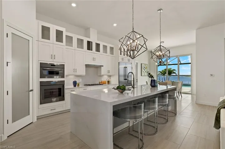 Gourmet Kitchen w/ luxury Thermador appliances, gas cooktop, luxury white cabinetry plus lighted upper cabinets, quartz counters & backsplash w/ oversized waterfall countertop on island, & walk-in pantry w/ frosted glass door