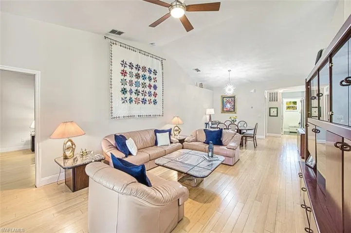Living area with a ceiling fan, visible vents, baseboards, lofted ceiling, and light wood-style floors