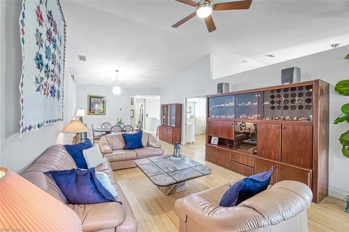 Living area featuring lofted ceiling, light wood-style floors, visible vents, and ceiling fan