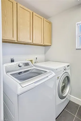 Laundry room featuring tile patterned flooring, washing machine and dryer, cabinet space, and baseboards
