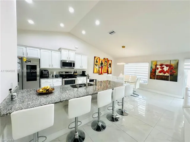 Kitchen with a breakfast bar, dark stone counters, stainless steel appliances, white cabinetry, and lofted ceiling