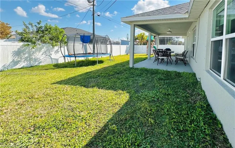 Fenced backyard with a patio area, a trampoline, a ceiling fan, and outdoor dining space
