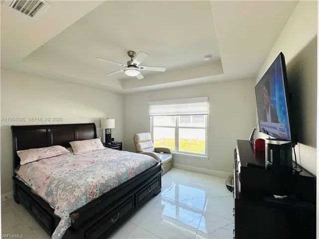 Bedroom featuring a raised ceiling, a ceiling fan, and light marble finish flooring