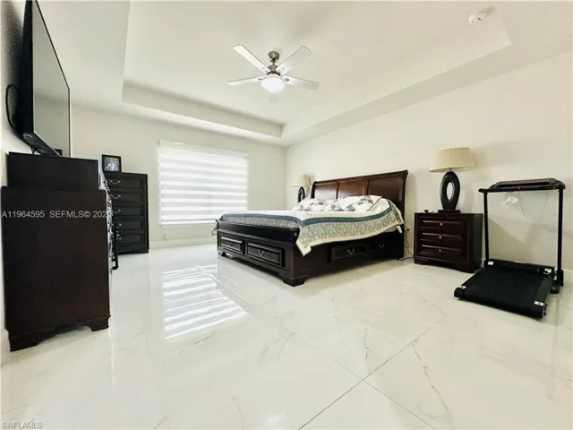Bedroom featuring a tray ceiling, light marble finish flooring, and ceiling fan