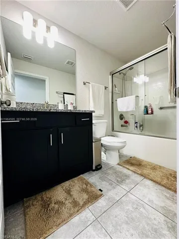Bathroom featuring enclosed tub / shower combo, vanity, light tile patterned flooring, and a textured ceiling