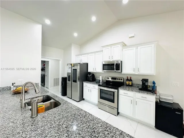 Kitchen featuring stainless steel appliances, light stone countertops, white cabinets, lofted ceiling, and washer / clothes dryer