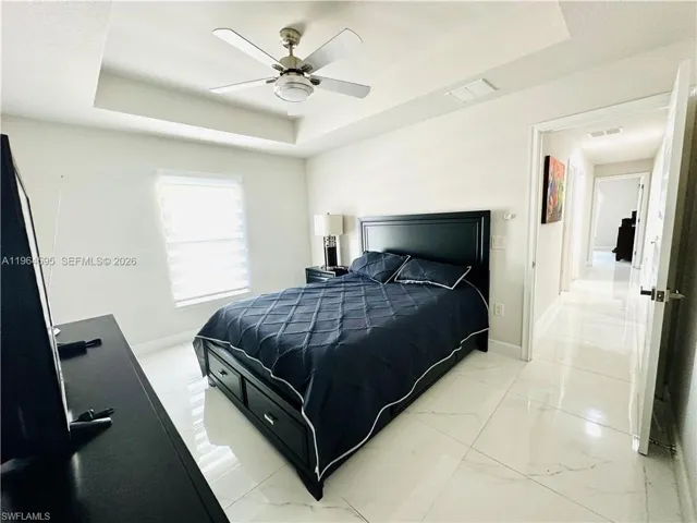 Bedroom with a tray ceiling, light marble finish floors, and ceiling fan