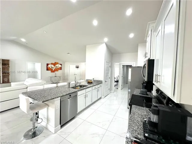 Kitchen featuring a breakfast bar area, a peninsula, dark stone counters, white cabinetry, and open floor plan
