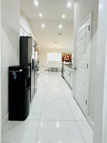 Kitchen with white cabinets, black fridge with ice dispenser, light stone counters, light marble finish floors, and vaulted ceiling