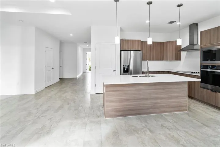 Kitchen featuring modern cabinets, brown cabinets, wall chimney range hood, stainless steel appliances, and pendant lighting