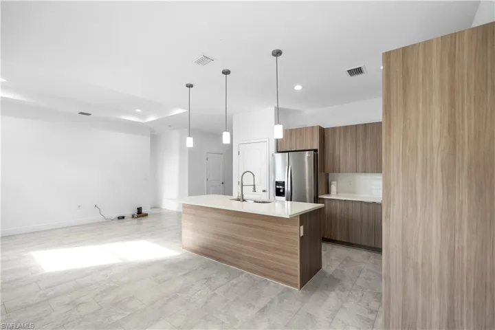 Kitchen with modern cabinets, decorative light fixtures, stainless steel refrigerator with ice dispenser, a kitchen island with sink, and light stone countertops