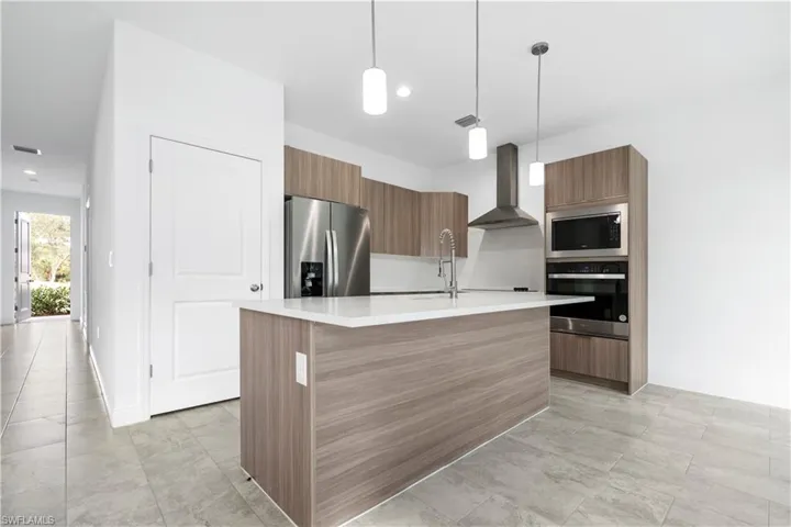 Kitchen featuring modern cabinets, brown cabinetry, stainless steel appliances, wall chimney range hood, and pendant lighting