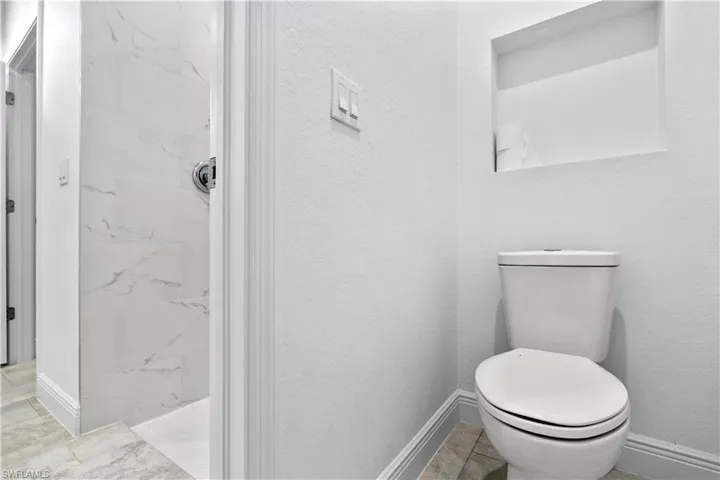 Bathroom with a marble finish shower and a textured wall