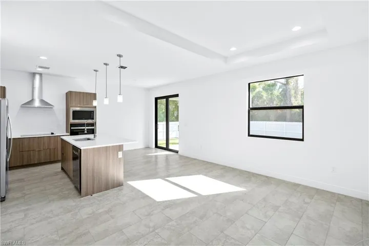 Kitchen with modern cabinets, pendant lighting, a kitchen island with sink, wall chimney range hood, and brown cabinetry