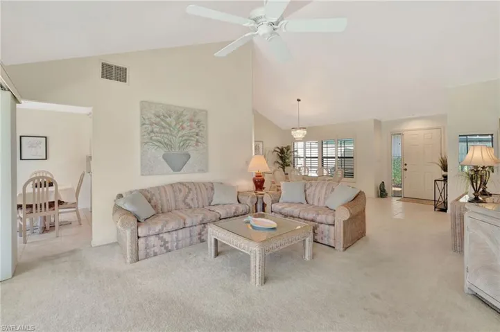 Living area featuring light carpet, high vaulted ceiling, and ceiling fan