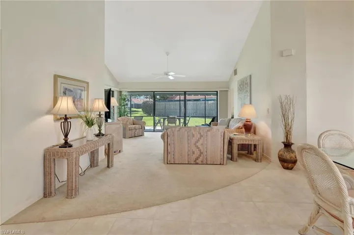 Carpeted living area with high vaulted ceiling, tile patterned floors, and ceiling fan
