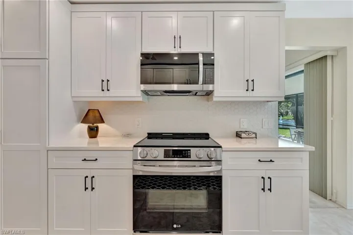 Kitchen featuring stainless steel appliances, white cabinetry, light countertops, and backsplash