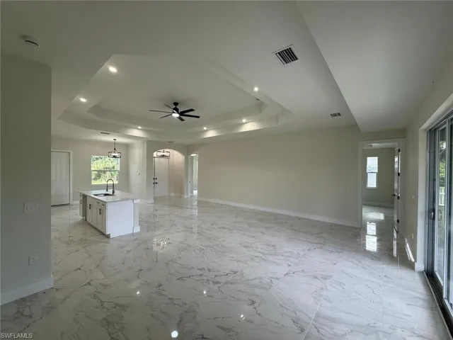 Empty room featuring a raised ceiling, arched walkways, plenty of natural light, and a ceiling fan