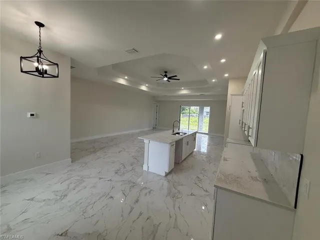 Kitchen with open floor plan, a tray ceiling, recessed lighting, a kitchen island with sink, and ceiling fan