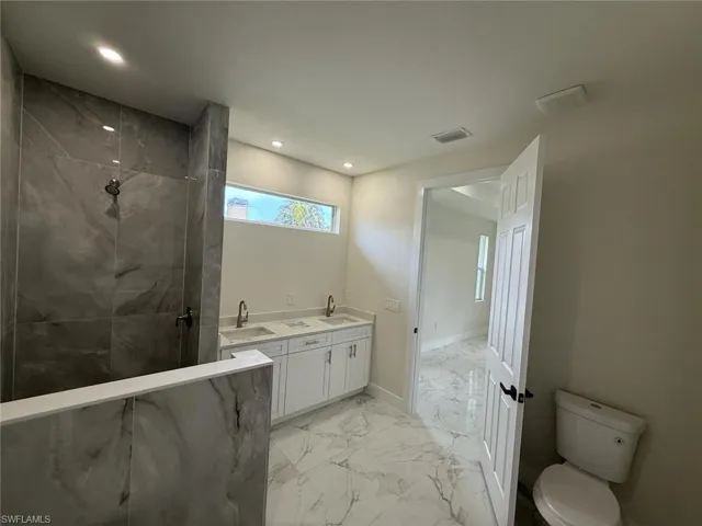 Full bathroom featuring marble look tile flooring, a marble finish shower, recessed lighting, and double vanity