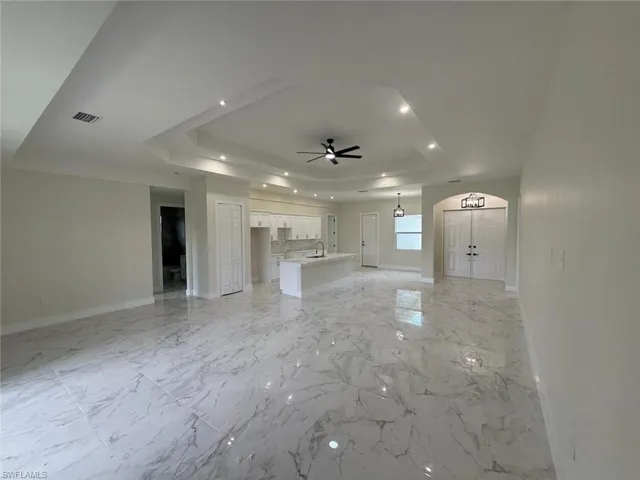 Unfurnished living room featuring a raised ceiling, a ceiling fan, and recessed lighting
