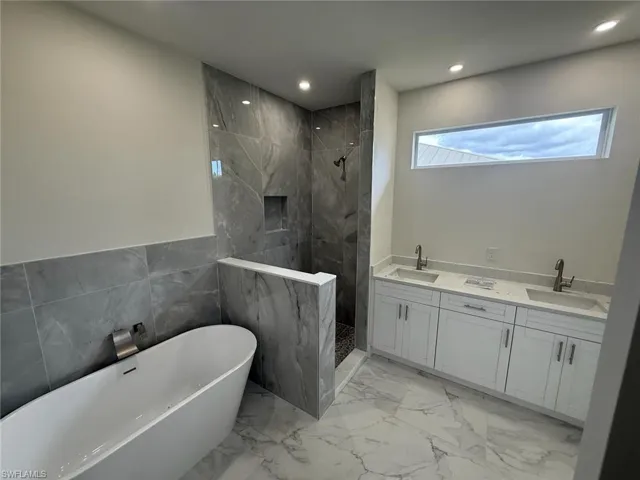 Bathroom featuring a marble finish shower, a freestanding tub, marble finish flooring, recessed lighting, and double vanity