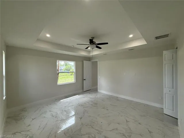 Unfurnished bedroom featuring a raised ceiling, recessed lighting, light marble finish flooring, and a ceiling fan
