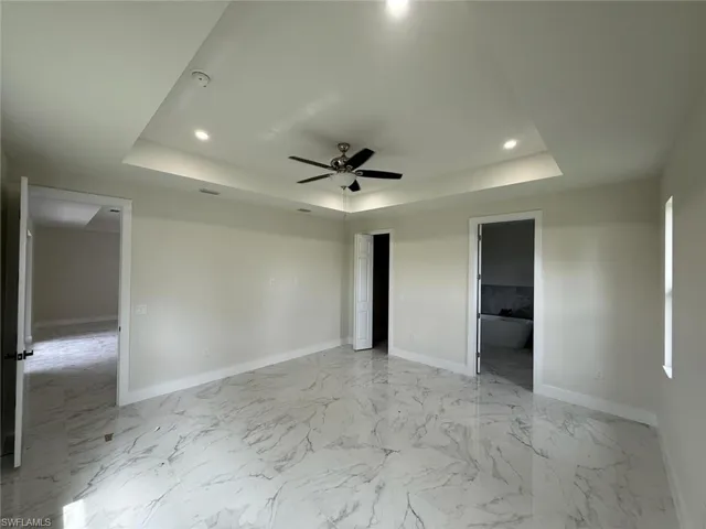 Unfurnished bedroom with a tray ceiling, light marble finish floors, recessed lighting, and ceiling fan