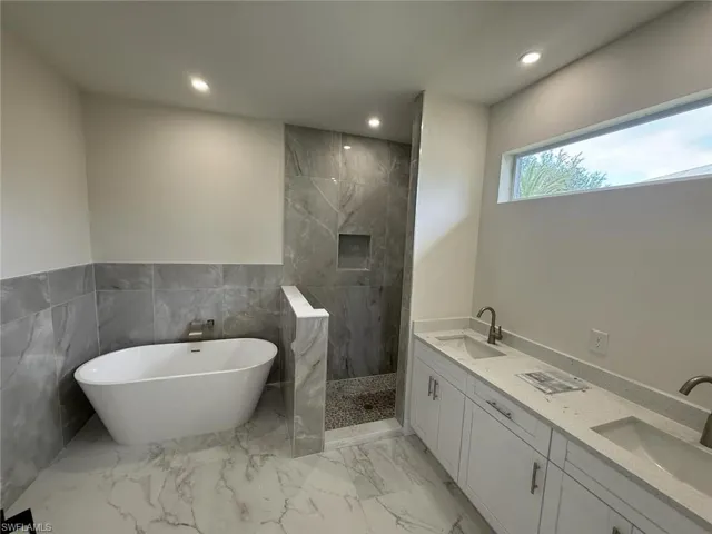 Bathroom featuring a soaking tub, recessed lighting, a marble finish shower, double vanity, and marble finish flooring