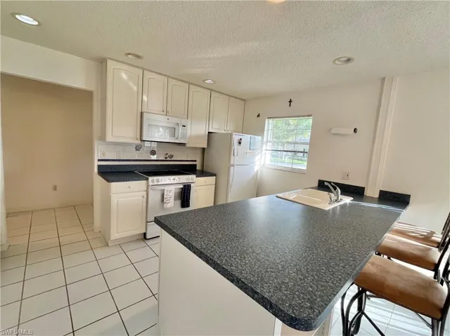Kitchen with white cabinetry, white appliances, a kitchen bar, sink, and kitchen peninsula