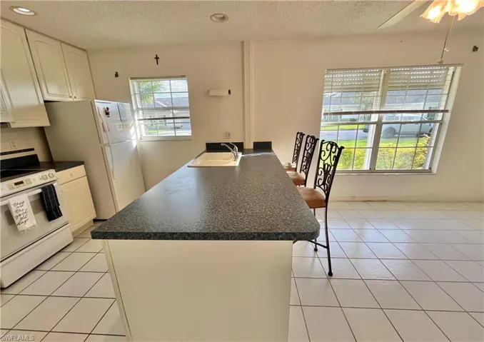 Kitchen with white appliances, sink, light tile patterned floors, and white cabinets
