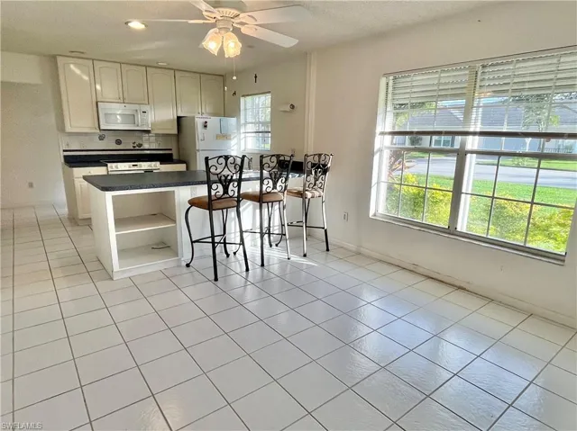 Kitchen with light tile patterned floors, decorative backsplash, a breakfast bar area, white appliances, and ceiling fan