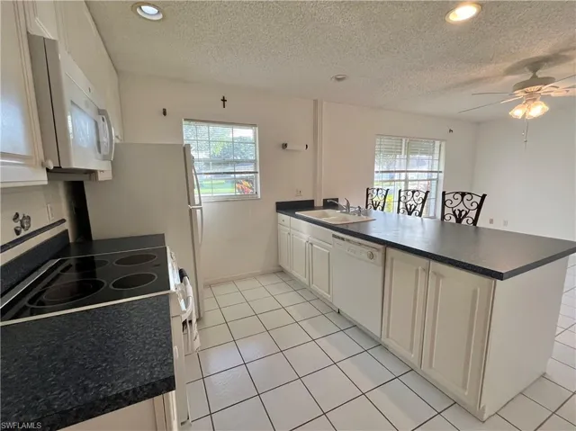 Kitchen featuring white appliances, a healthy amount of sunlight, sink, and kitchen peninsula