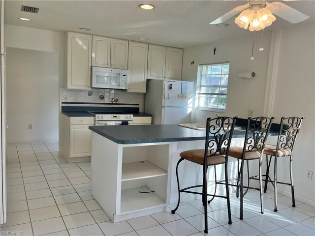 Kitchen with white cabinetry, a textured ceiling, light tile patterned floors, decorative backsplash, and white appliances