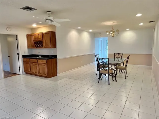 Dining space with sink, light tile patterned floors, and ceiling fan with notable chandelier