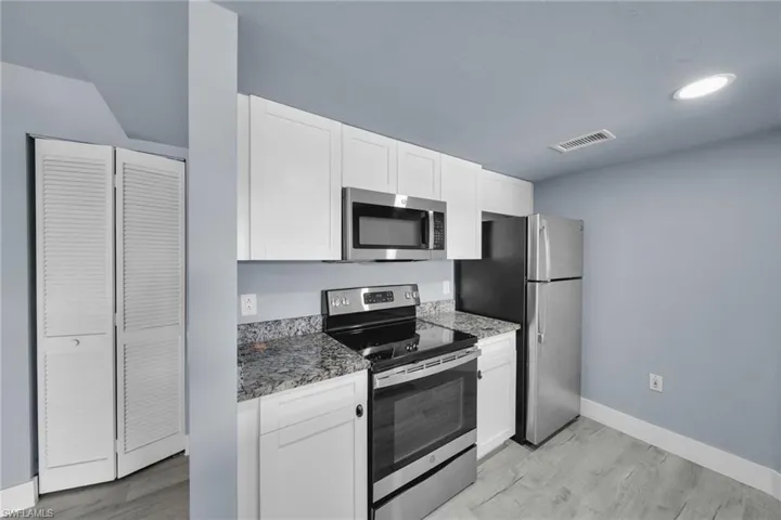 Kitchen featuring white cabinetry, speckled countertops, stainless steel appliances, and wood-finish flooring